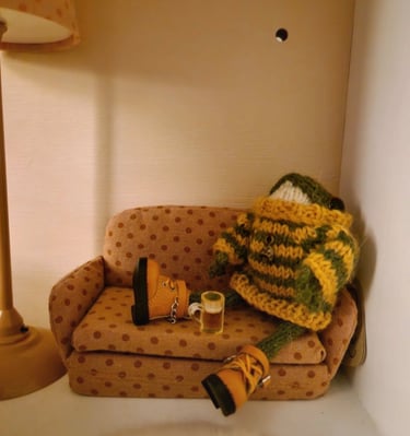a couch with a sitting small knitted frog holding a pint of beer