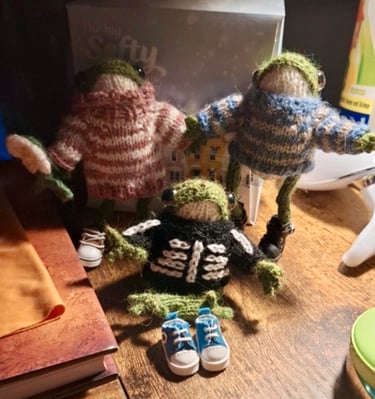 a group of knitted little froggies in jumpers sitting on a table