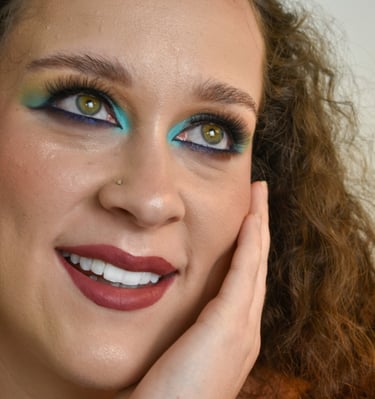 Una mujer con cabello rizado que usa sombras de ojos azules y amarillas vibrantes y un lápiz labial