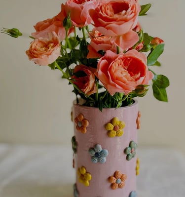 A handmade vase with colourful flower decoration filled with roses
