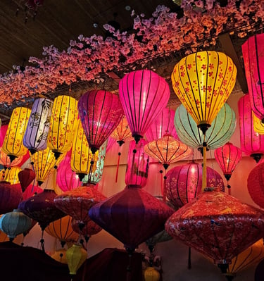 Vibrant colorful Vietnamese silk lanterns hanging under pink cherry blossoms at a cultural festival.
