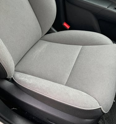 Close-up of a leather car seat before deep cleaning, showing stains and wear.