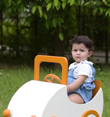 Toddler playing in a white and orange wooden toy car. Milestone photography
