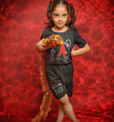 Young girl in black outfit holding a plush snake toy against a red studio background.