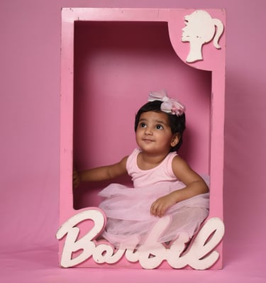 Baby girl in a pink tutu posing inside a Barbie-themed toy box for a creative photoshoot. Wonderpose