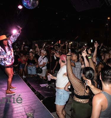 black rapper on stage, arms outstretched while audience close to stage claps with arms raised