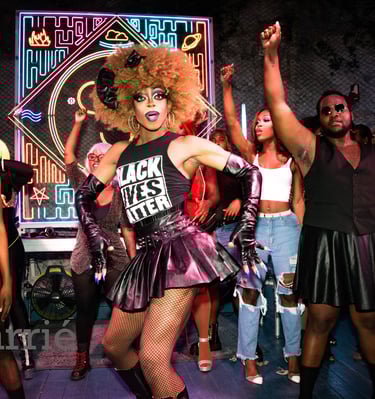 drag queen in "black lives matter" shirt dances toward audience surrounded by dancers.