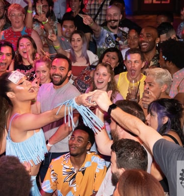 drag performer with dollar bill stuck to forehead in the middle of a crowd accepting tips 