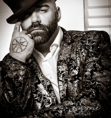 black & white portrait of man in top hat with feather looking seductively wearing shiny blazer