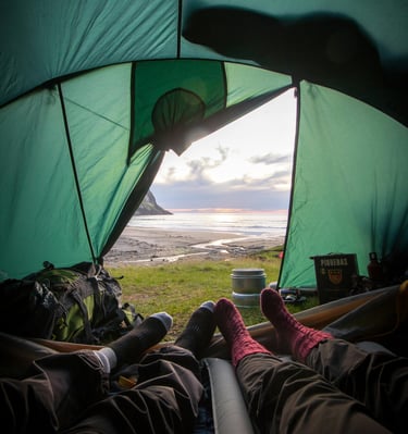 people laying in a tent camping with their feet up next to the sea