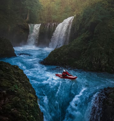 an adventurous man in a red kayak kayaking in the middle of a mountain river waterfall