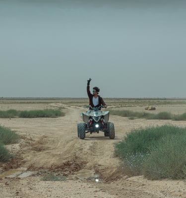 a man riding a quad - atv in the desert with his hands up peace sign