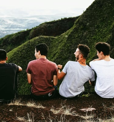 a group of people friends sitting on a hill in the green mountains laughing together