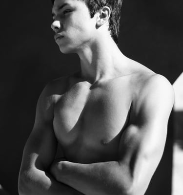a young muscular man standing looking aloof with folded arms