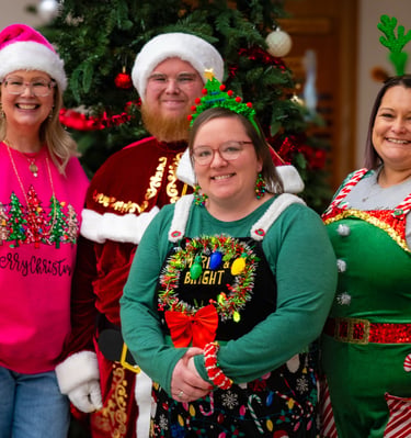 Four people wearing festive Christmas outfits and Santa hats posing in front of a X-mas tree. Athens