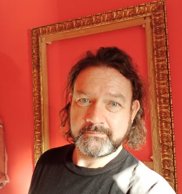 The writer Ian Farnes, framed by a gold picture frame on a red background. he looks at the camera