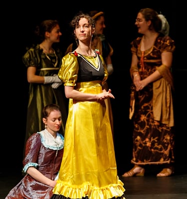 Aude Fy, en costume d'époque jaune dans une pièce de théâtre, interprétant une cantatrice