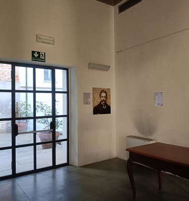 Nietzche a glass door, a wooden desk, and a portrait hanging on a white wall.
