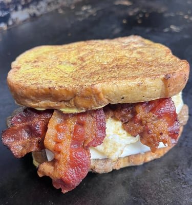 Hearty bacon breakfast sandwich loaded with crispy bacon, scrambled eggs, and melted cheddar on toasted bread—Slap Yo Self’s 