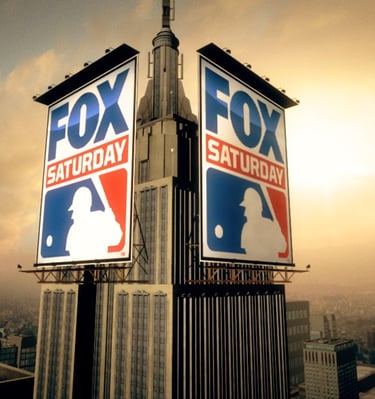 MLB Fox Saturday banners hang on a skyscraper with a sunset cityscape in the background
