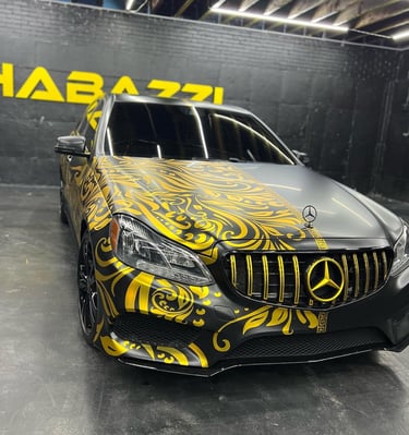 Custom matte black Mercedes-Benz with a gold baroque patterned vinyl wrap and a matching gold grille.