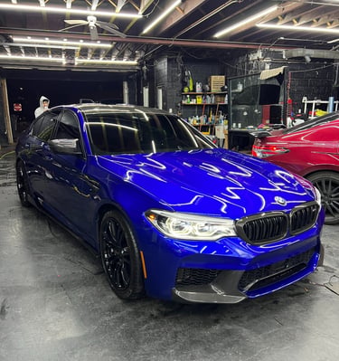 Polished blue BMW M5 sports sedan with black wheels inside a professional auto detailing shop.