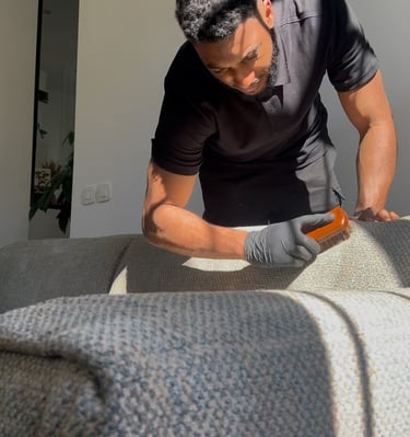 a man in a black shirt and gloves is cleaning a couch