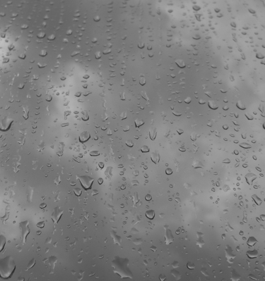 Gotas de lluvia sobre un cristal en blanco y negro con cielo nublado.