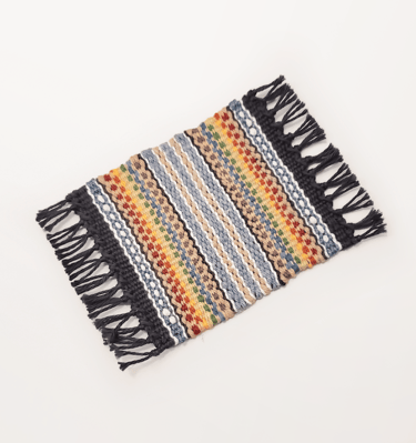 a hand-woven mug rug coaster with muted pride rainbow colours