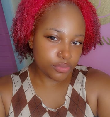 A young woman with rosy pink natural curls, styled in a short, voluminous shape. Her glowing skin, subtle makeup, and nose pi