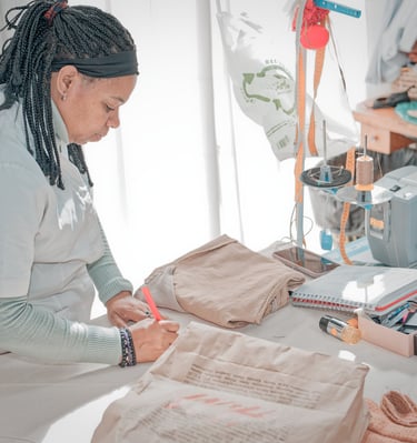 Modista trabajando en un taller de costura, marcando una prenda doblada sobre la mesa junto a una má