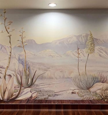 Full view on a desert mural, painted in soft beige, green and lilac colours, overlooking mountains, boulders and desert plant
