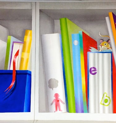 Segment of school library mural depicting brightly coloured hand-painted books, an blue toy box and a little mouse reading.