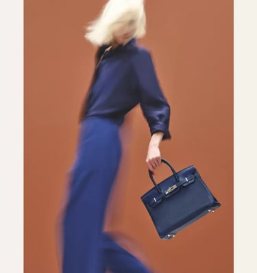Model in motion holding an Hermes Birkin navy blue luxury handbag against a vibrant backdrop.