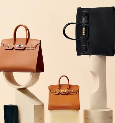 Hermes Birkin bags, Luxury tan and black handbags displayed on minimalist stone stands.