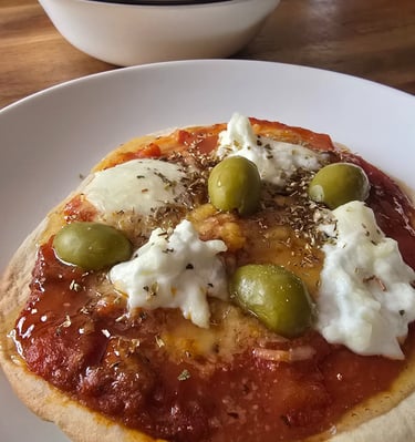 Pan pita con pasta de tomate y encima queso burrata y olivas verdes y oregano encima delciosos