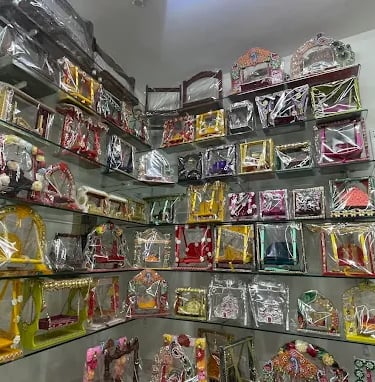 A collection of colorful decorative wooden swings for Hindu idols displayed on glass shelves in a shop.