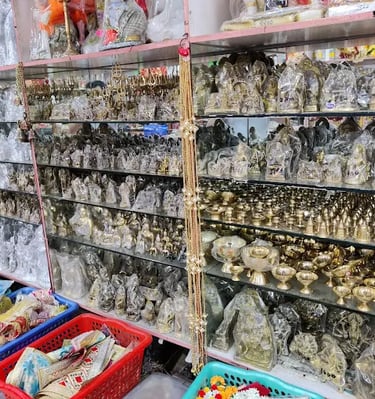 Brass and silver plated Hindu deity idols and puja items displayed on glass shelves in a shop.