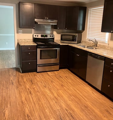 Modern kitchen with dark wood cabinets, granite countertops, and stainless steel appliances over hardwood floors.