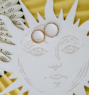 Two gold wedding bands resting on a white sun illustration with a yellow background.