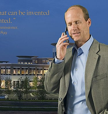 A businessman talks on a mobile phone near a Sprint logo and modern office building.