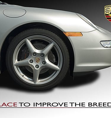 Close-up of a silver Porsche 911 front wheel and alloy rim with the brand logo and race slogan.