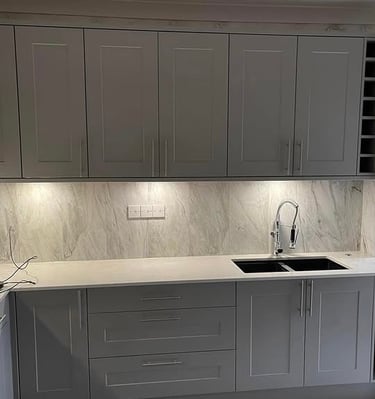 Modern grey shaker kitchen cabinets with marble backsplash and under-cabinet lighting.