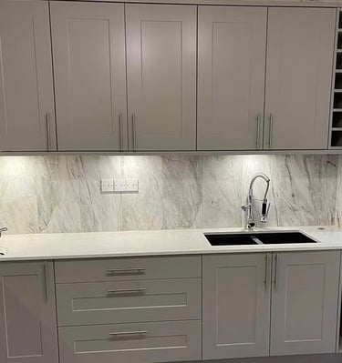 Modern grey kitchen cabinets with marble backsplash, white countertops, and integrated appliances. 