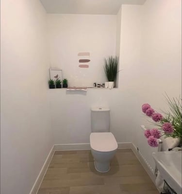 Modern minimalist bathroom featuring a white toilet, light wood flooring, and artificial plants.