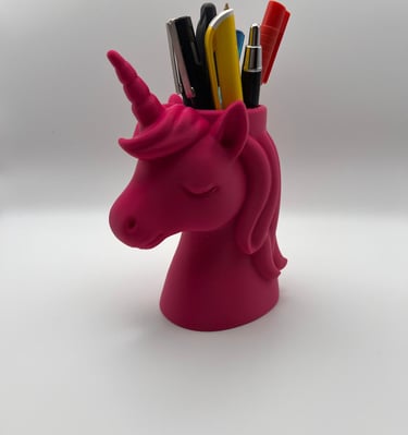 A pink unicorn head pencil holder filled with colorful pens and office supplies on a white background.