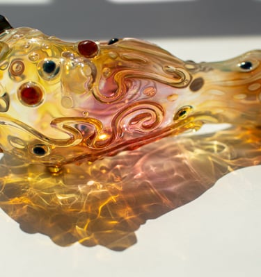Handblown glass spoon pipe with intricate amber fumed patterns and colorful glass dots for smoking.