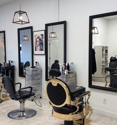 Modern hair salon interior featuring gold and black barber chairs, large wall mirrors, and glass display shelves.