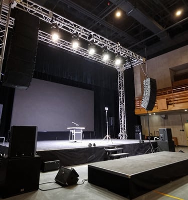 Professional stage setup with lighting truss, line array speakers, and a podium for live events.