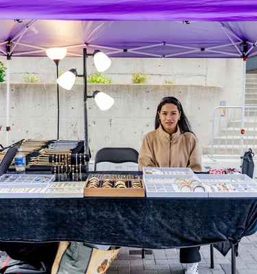 A female artisan selling handmade jewelry at an outdoor Afro Fiesta Festival vendor booth.